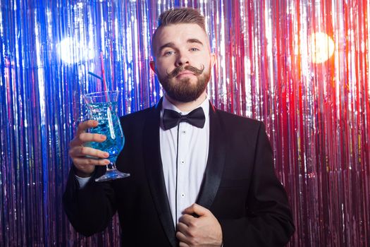 Portrait of elegant handsome man in a expensive suit holds blue cocktail on shiny background