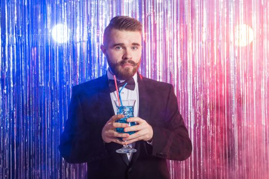 Portrait of elegant handsome man in a expensive suit holds blue cocktail on shiny background