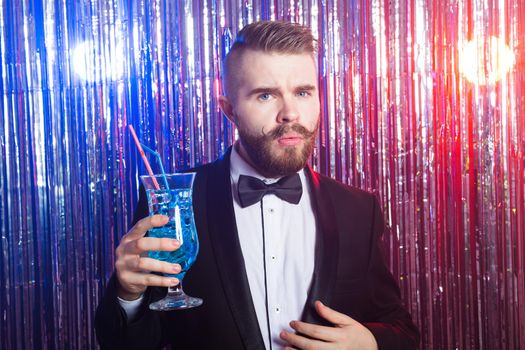 Portrait of elegant handsome man in a expensive suit holds blue cocktail on shiny background