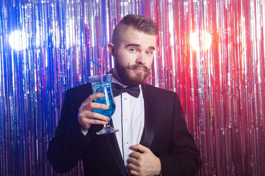 Portrait of elegant handsome man in a expensive suit holds blue cocktail on shiny background