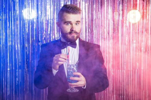 Portrait of elegant handsome man in a expensive suit holds blue cocktail on shiny background