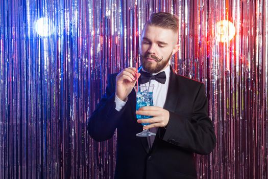 Portrait of elegant handsome man in a expensive suit holds blue cocktail on shiny background