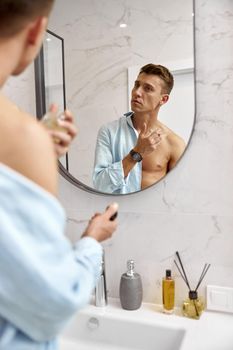 Photo of adult caucasian beautiful man in front of mirror in light modern bathroom