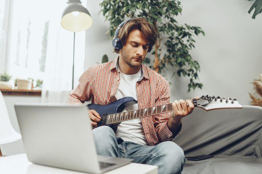 Man playing electric guitar and recording music into laptop at home