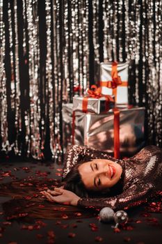 Top view of a girl lying in shiny clothes on the floor in confetti in the form of hearts and gifts.