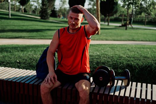 Cheerful male athlete in the park sits on a bench. High quality photo