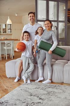 Full length portrait of happy parents with son and daughter standing in living room with equipment for training