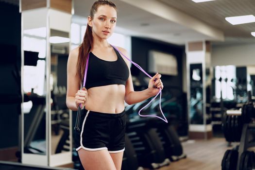 Portrait of a pretty fit girl with jumping rope standing in a gym