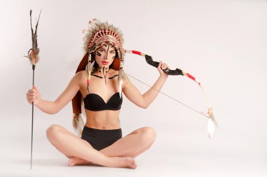 the woman in the image of indigenous peoples of America with a bow and arrow poses sitting on a light background