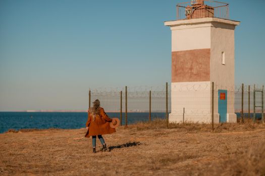 A woman walking along the coast near the sea. An elegant lady in a brown coat and a hat with fashionable makeup walks on the seashore.