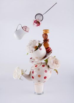 balancing structure of polka dot teapot, cup and saucers with macaroons and levitating milk jug and tea strainer blooming with flowers