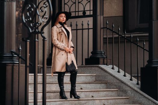 Stylish young woman in a beige coat in a black hat on a city street. Women's street fashion. Autumn clothing.Urban style.