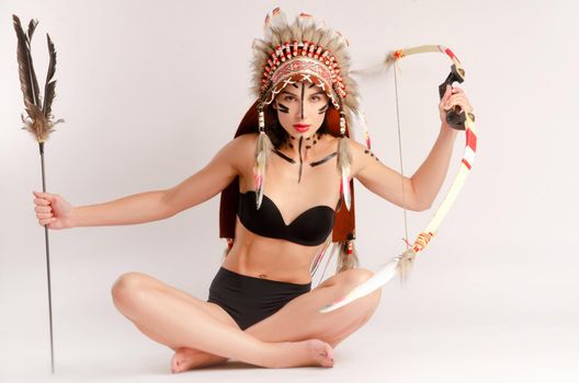 the woman in the image of indigenous peoples of America with a bow and arrow poses sitting on a light background