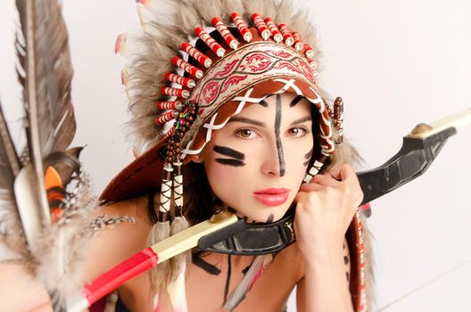the woman in the image of indigenous peoples of America with a bow and arrow poses sitting on a light background