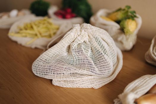 Closed a reusable grocery bag with vegetables on a table at home. Mesh cotton with vegetables.