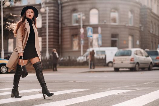 Stylish young woman in a beige coat in a black hat on a city street. Women's street fashion. Autumn clothing.Urban style.