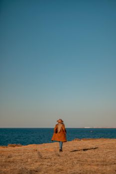 A woman walking along the coast near the sea. An elegant lady in a brown coat with fashionable makeup walks on the seashore.