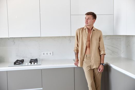 Happy handsome man is standing on minimalistic kitchen and smiling