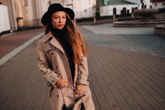 Stylish young woman in a beige coat in a black hat on a city street. Women's street fashion. Autumn clothing.Urban style.