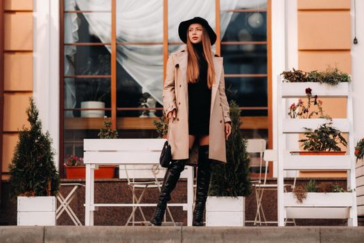 Stylish young woman in a beige coat in a black hat on a city street. Women's street fashion. Autumn clothing.Urban style.