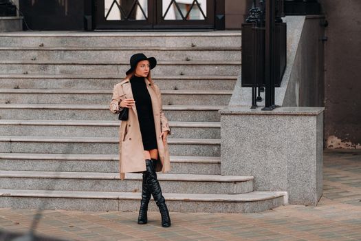 Stylish young woman in a beige coat in a black hat on a city street. Women's street fashion. Autumn clothing.Urban style.