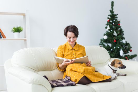 christmas, holidays and people concept - happy young woman reading book at home