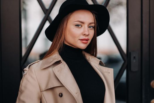 Stylish young woman in a beige coat in a black hat on a city street. Women's street fashion. Autumn clothing.Urban style.