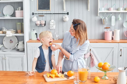 Healthy food, fresh fruit, juicy oranges. Mother and son are smiling while having a breakfast in kitchen. Bright morning in the kitchen