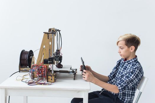 Education, children, technology concept - teen boy is printing on 3d printer