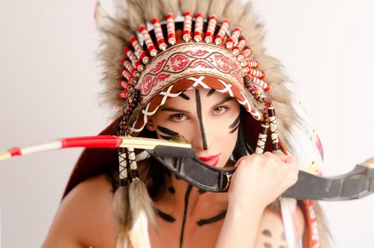 the woman in the image of indigenous peoples of America with a bow and arrow poses sitting on a light background