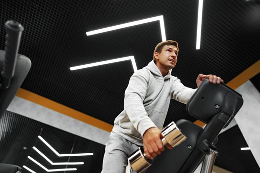 Determined handsome young male working out in gym with dumbbells, close up