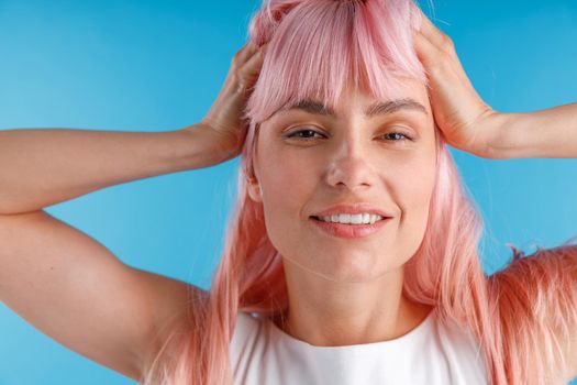 Close up portrait of beautiful female model with pink hair smiling at camera while posing isolated over blue studio background. Beauty, hair care concept