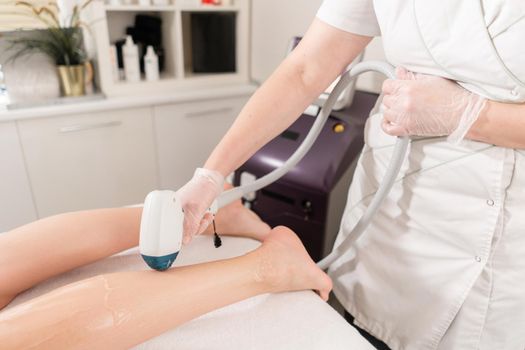 Doctor cosmetologist makes the procedure a young girl brunette. Laser epilation and cosmetology. Hair removal on ladies legs. at cosmetic beauty spa clinic