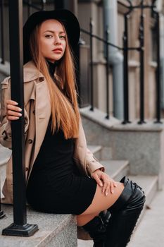 Stylish young woman in a beige coat in a black hat on a city street. Women's street fashion. Autumn clothing.Urban style.