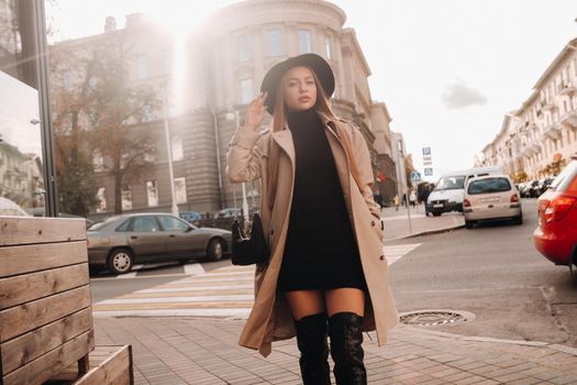 Stylish young woman in a beige coat in a black hat on a city street. Women's street fashion. Autumn clothing.Urban style.