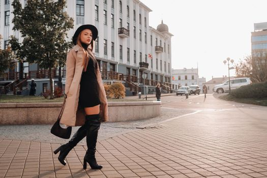 Stylish young woman in a beige coat in a black hat on a city street. Women's street fashion. Autumn clothing.Urban style.