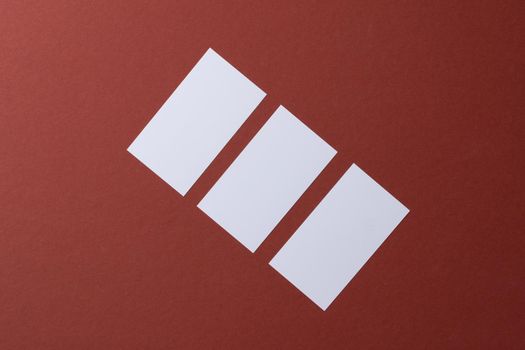 Blank white business cards on burgundy paper background, top view