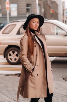 Stylish young woman in a beige coat in a black hat on a city street. Women's street fashion. Autumn clothing.Urban style.