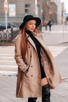 Stylish young woman in a beige coat in a black hat on a city street. Women's street fashion. Autumn clothing.Urban style.