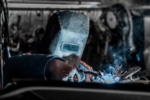 Welder industrial worker in the protective shield is engaged in welding and metal work at the plant.