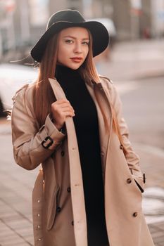 Stylish young woman in a beige coat in a black hat on a city street. Women's street fashion. Autumn clothing.Urban style.