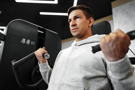 Young fit bodybuilder man doing arms workout training in the gym on machine, close up