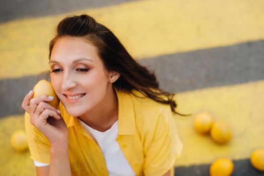 a girl with lemons in a yellow shirt, shorts and black shoes sits on a yellow pedestrian crossing in the city. The lemon mood.