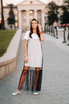 A girl with long hair with red earrings in white clothes walks around the city.The model holds her hair in her hands and smiles.