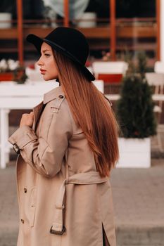 Stylish young woman in a beige coat in a black hat on a city street. Women's street fashion. Autumn clothing.Urban style.