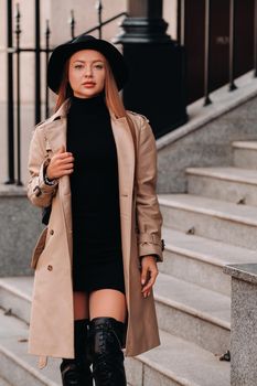 Stylish young woman in a beige coat in a black hat on a city street. Women's street fashion. Autumn clothing.Urban style.