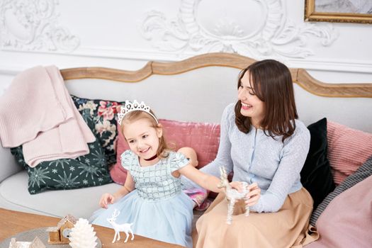 Cheerful mom embraces her cute baby daughter . Parent and little child having fun near Christmas tree indoors. Loving family Merry Christmas and Happy New Year.