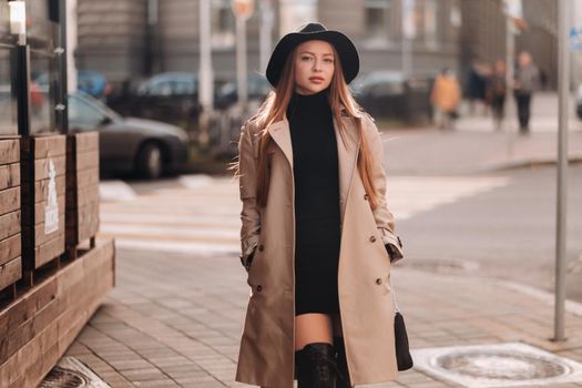 Stylish young woman in a beige coat in a black hat on a city street. Women's street fashion. Autumn clothing.Urban style.