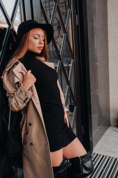 Stylish young woman in a beige coat in a black hat on a city street. Women's street fashion. Autumn clothing.Urban style.