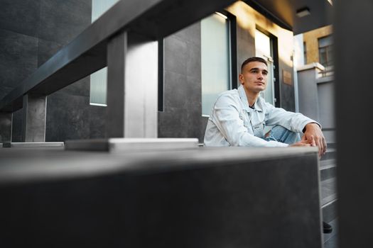 Young casual man sitting on stairs alone on city street
